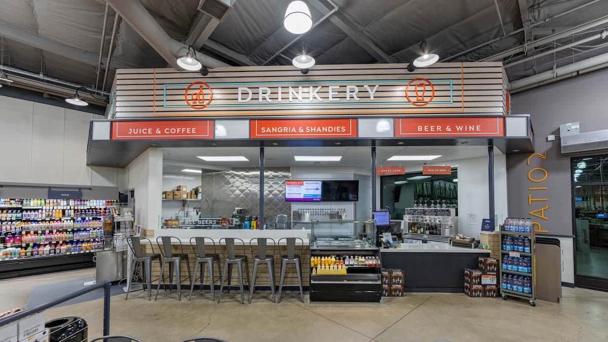 Lucky stores grocery sign. DRINKERY in large white letters against a slat wall background. Flanked by round icons for wine and beer. Below are additional signs.